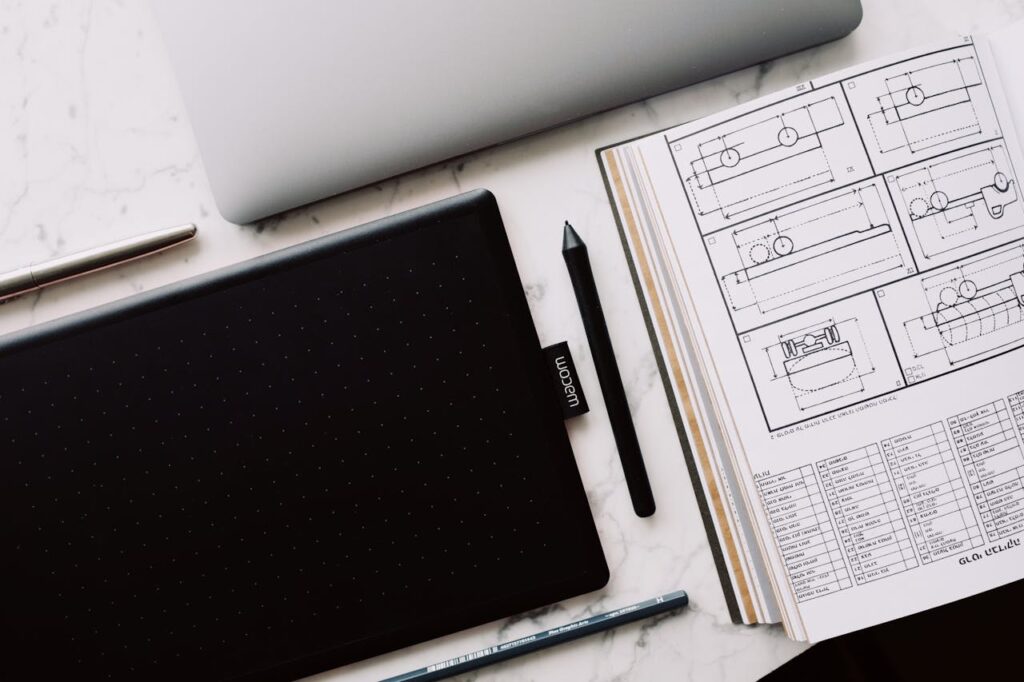 Graphic tablet and open book with drawing located on marble table